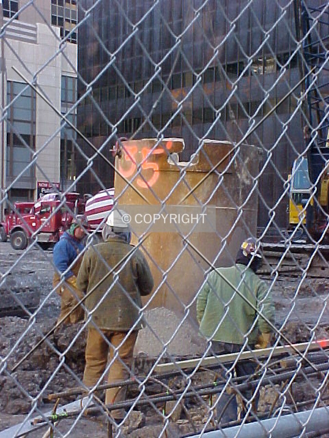 Construction workers guiding a steel tube into a freshly drilled caisson hole