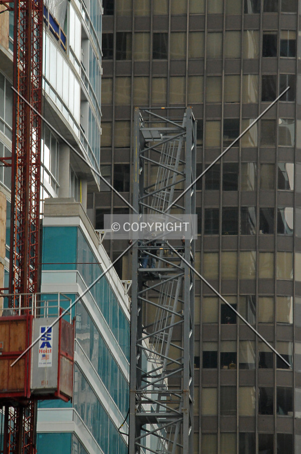 Workers removing bolts to disassemble sections of the tower crane shaft