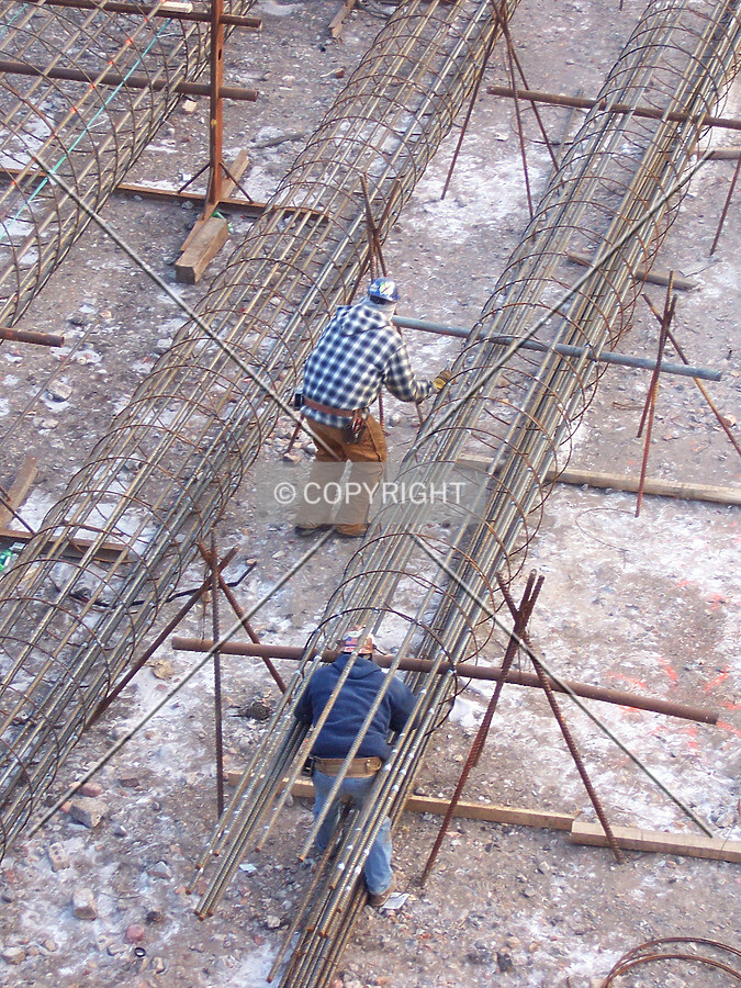 Two workers assembling rebar cages in the northeast corner of the site