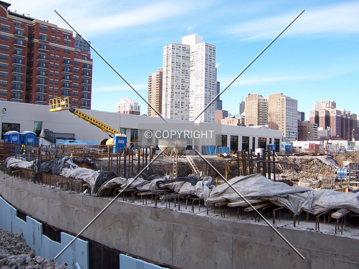Looking northwest into the site with foundation walls and reinforcing bar in the foreground