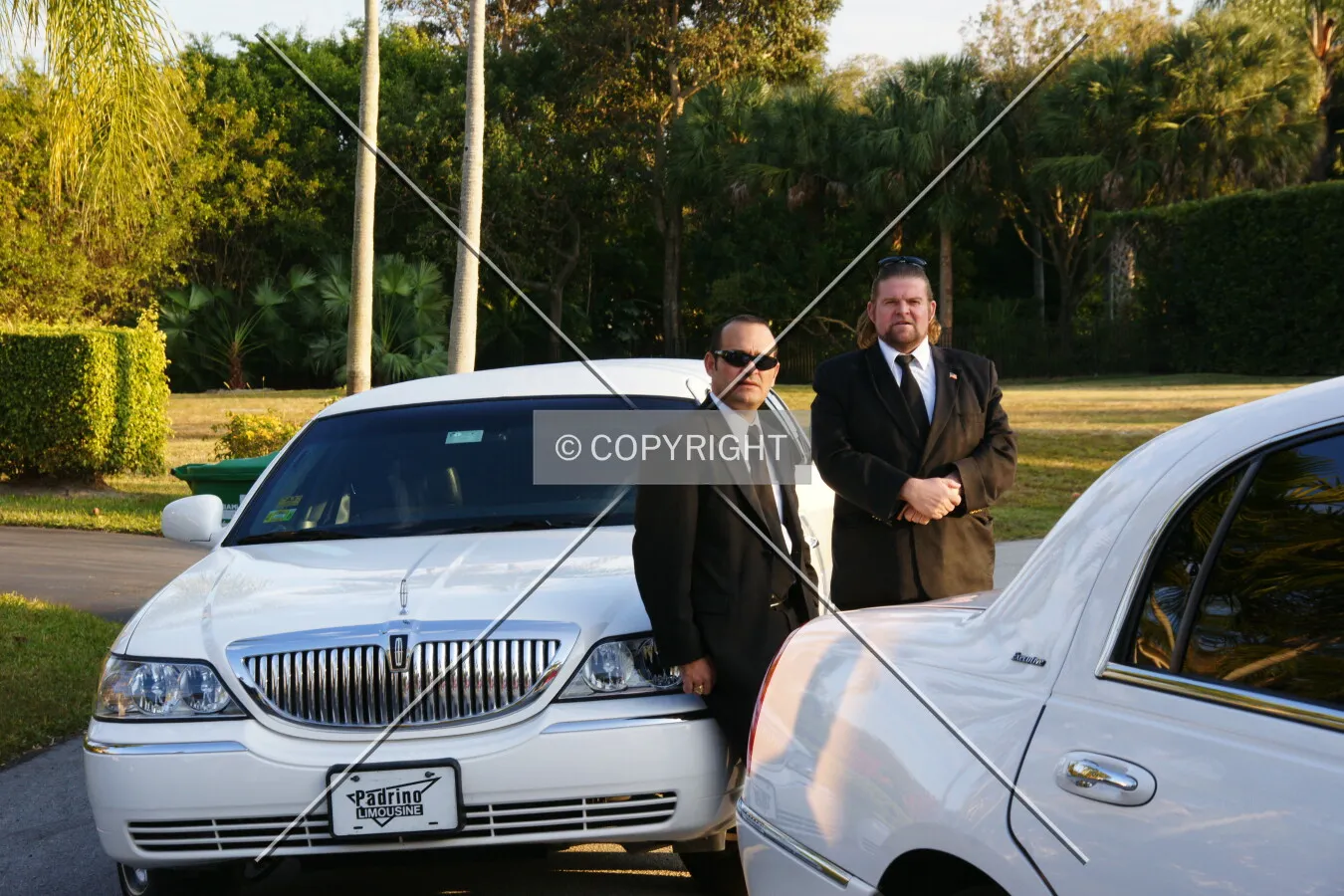 Two bodyguards are standing at two stretch limousines