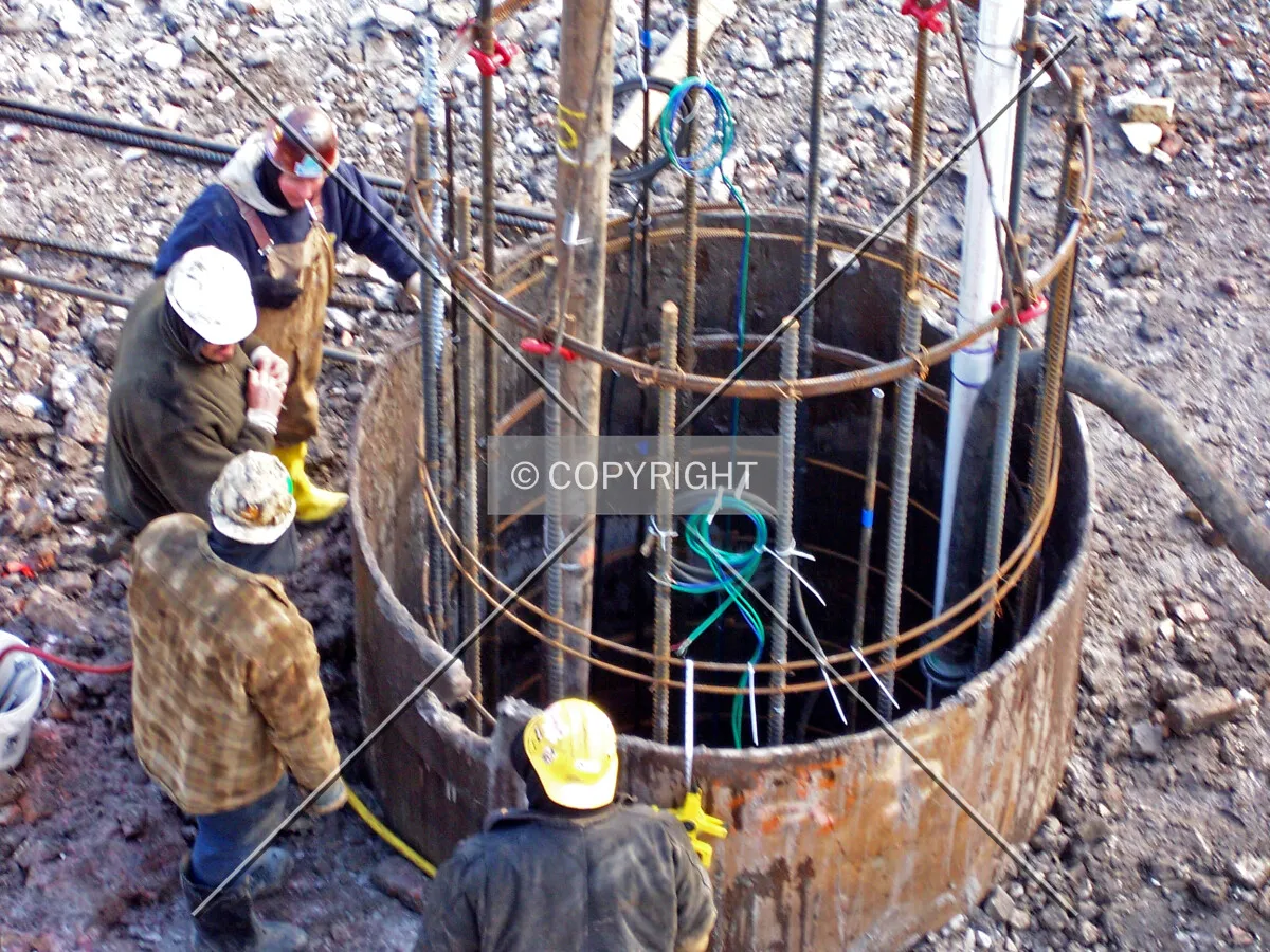 Workers watching a caisson shaft while it is pumped full of concrete