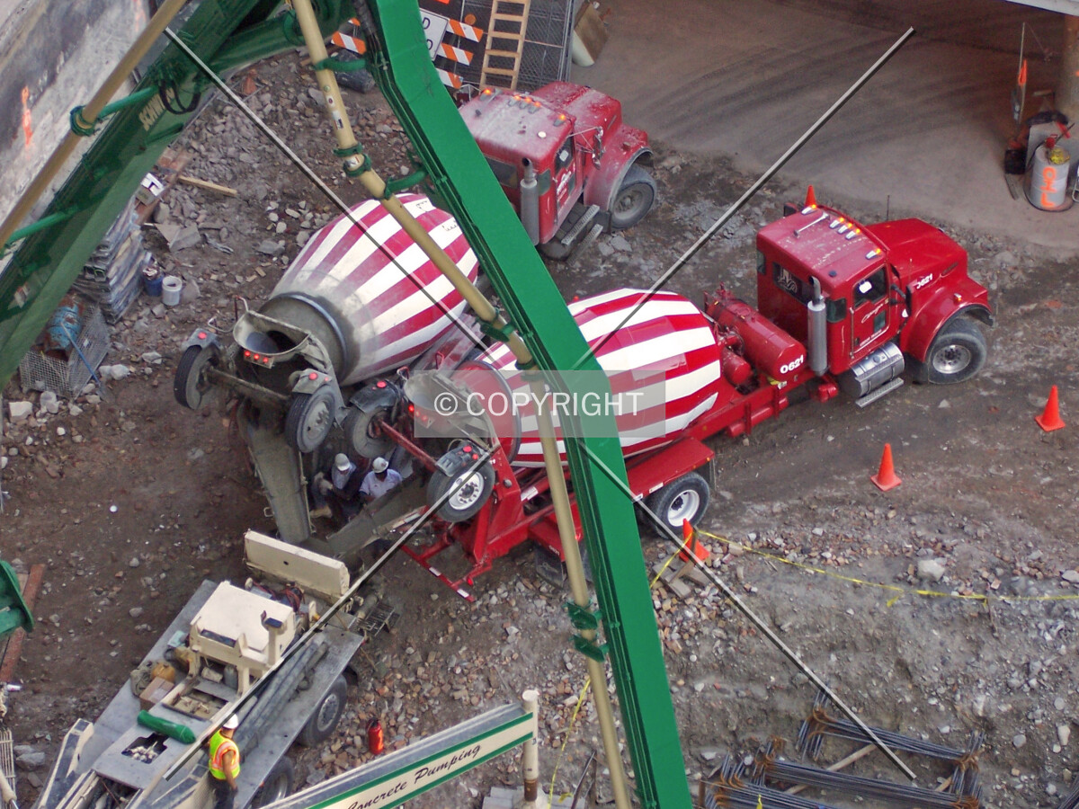 Two Ozinga concrete trucks dumping their loads into the concrete pump, which is then sent to the foundation mat below through a hose attached to the green mechanical boom