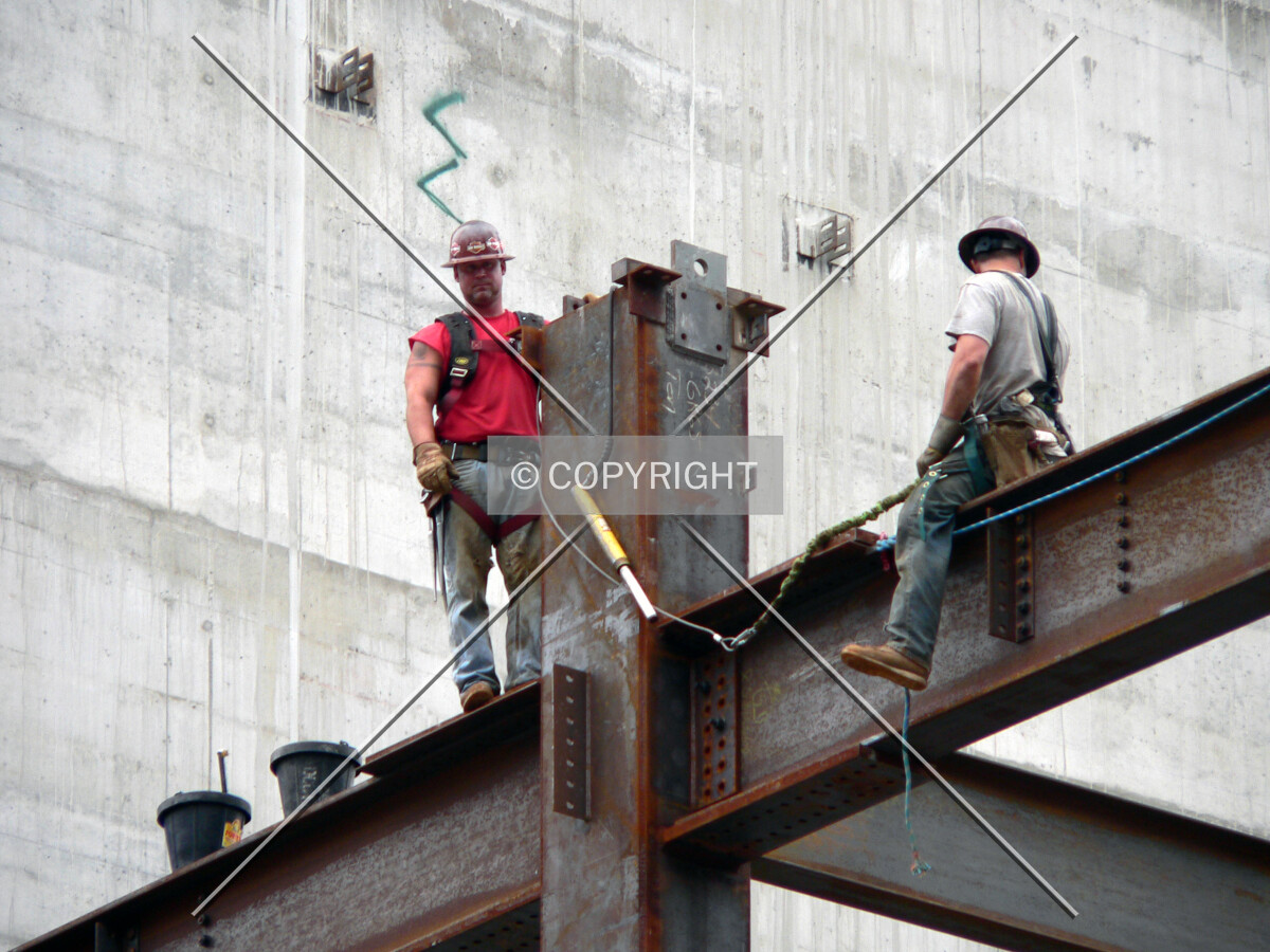 Construction workers straddling a beam waiting for a delivery