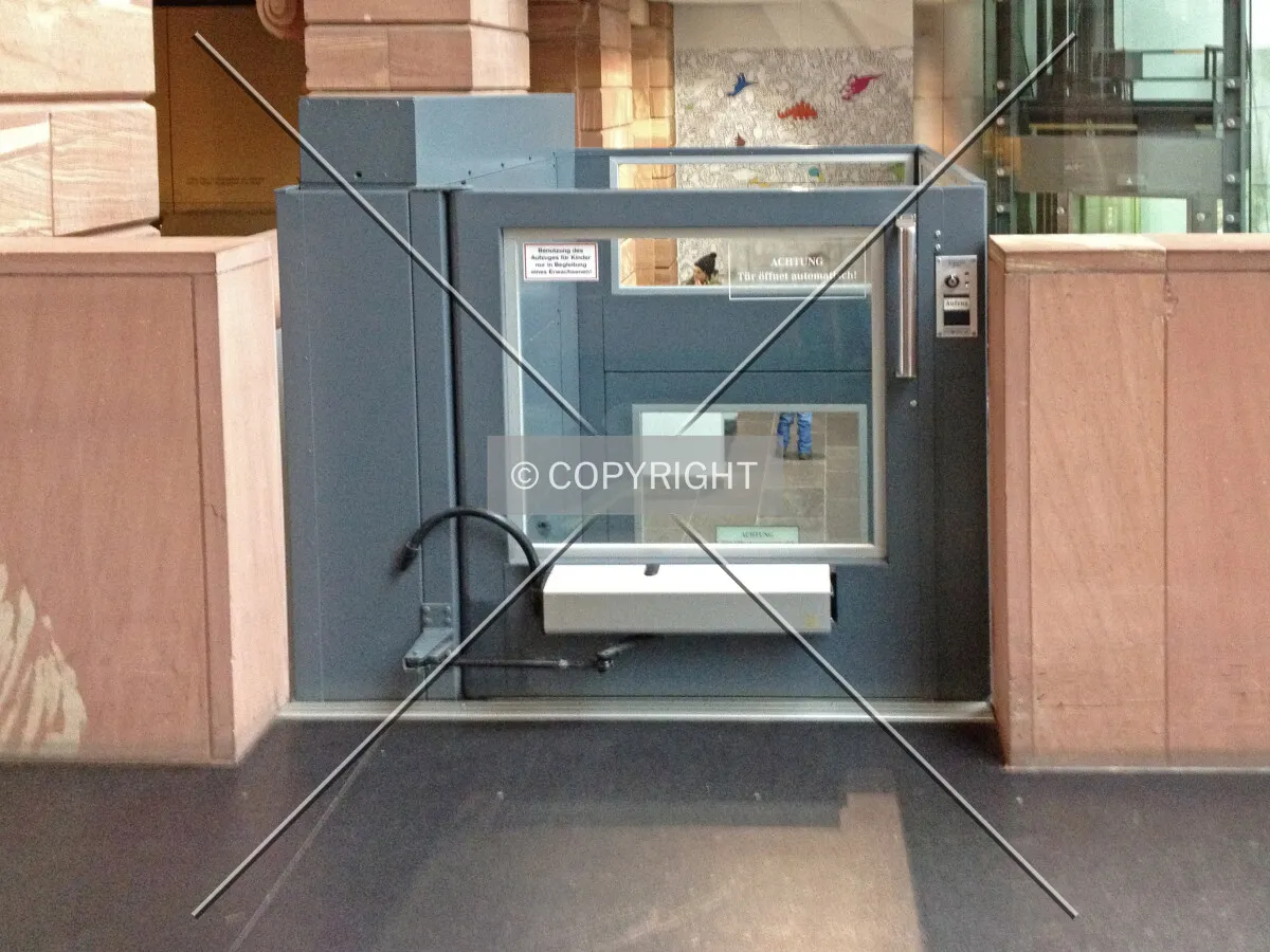 An elevator inside a building without a roof carrying wheelchair drivers