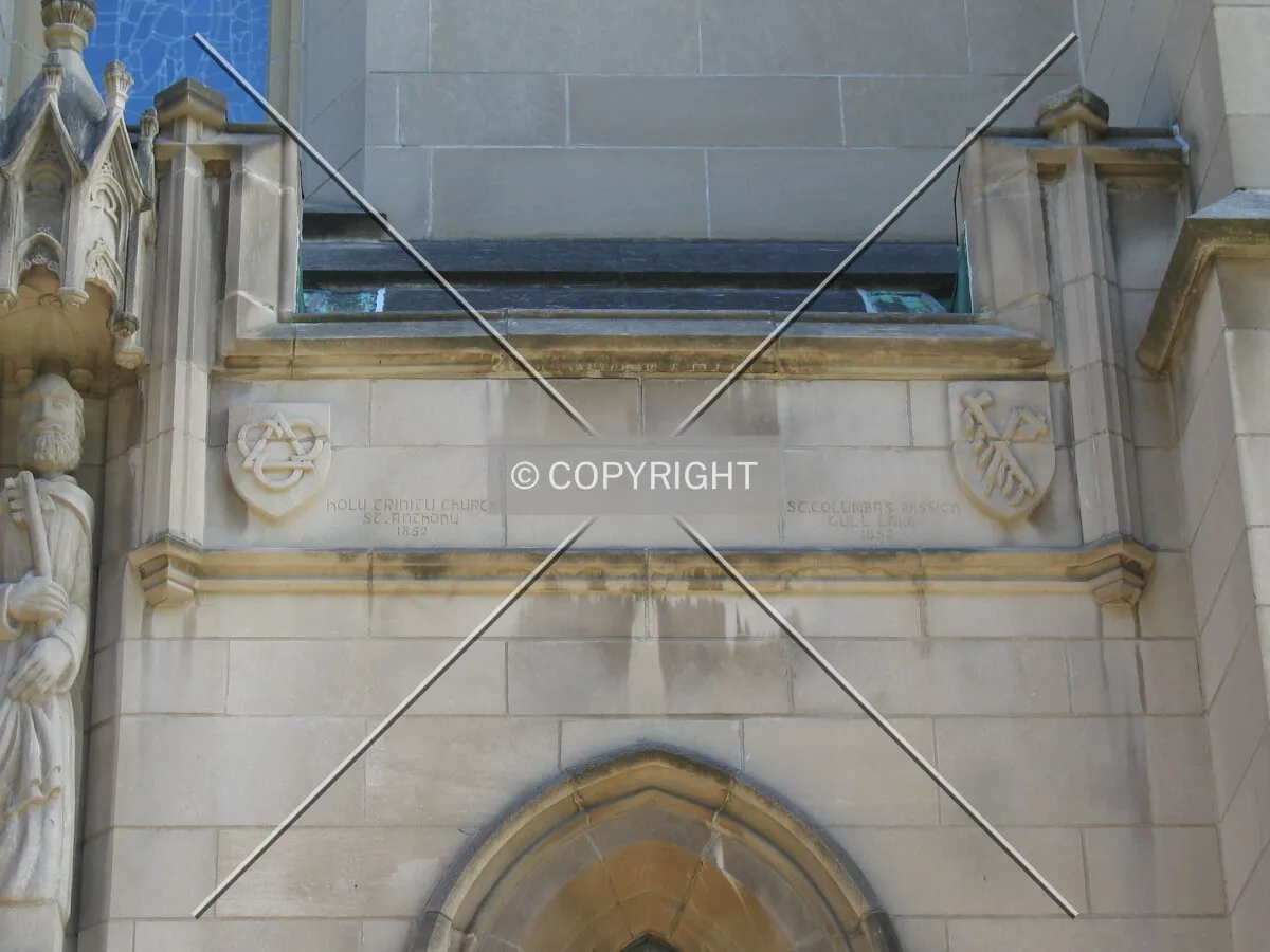 Two shields to the right of the entrance, representing Holy Trinity Church in St. Anthony and St. Columba's Mission in Gull Lake