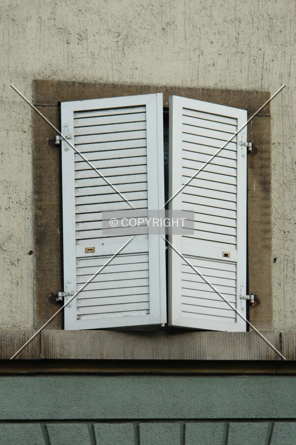 A window in an old building with 2 white window shades which can be flapped