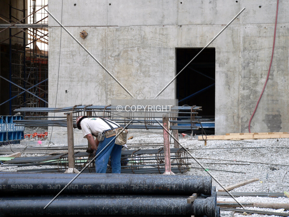 Worker building a rebar column cage with the core rising in the background
