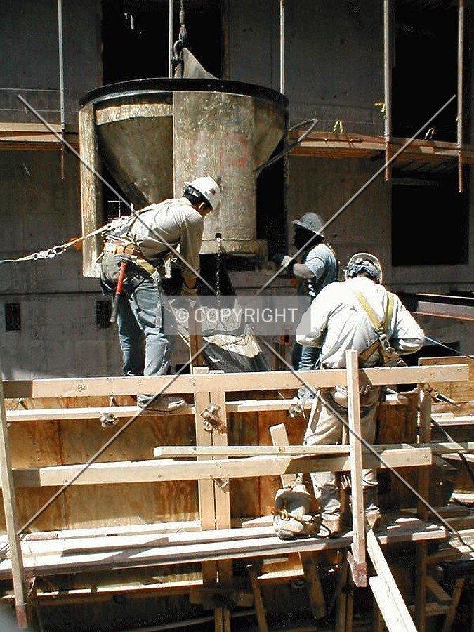 Tethered construction workers pouring cement into mold