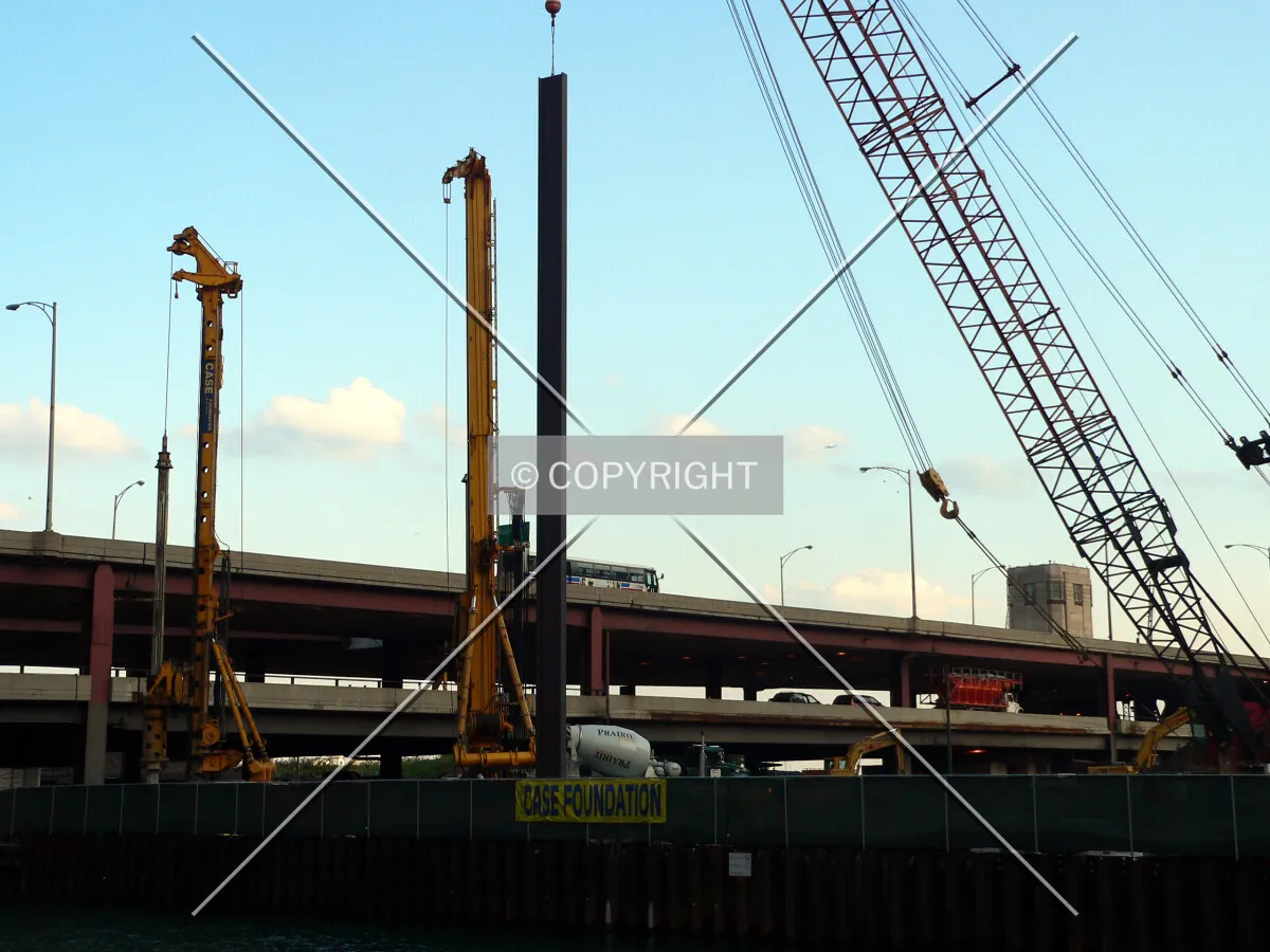 View to the southeast as an I-beam is lowered into position for the secant wall along Ogden Slip