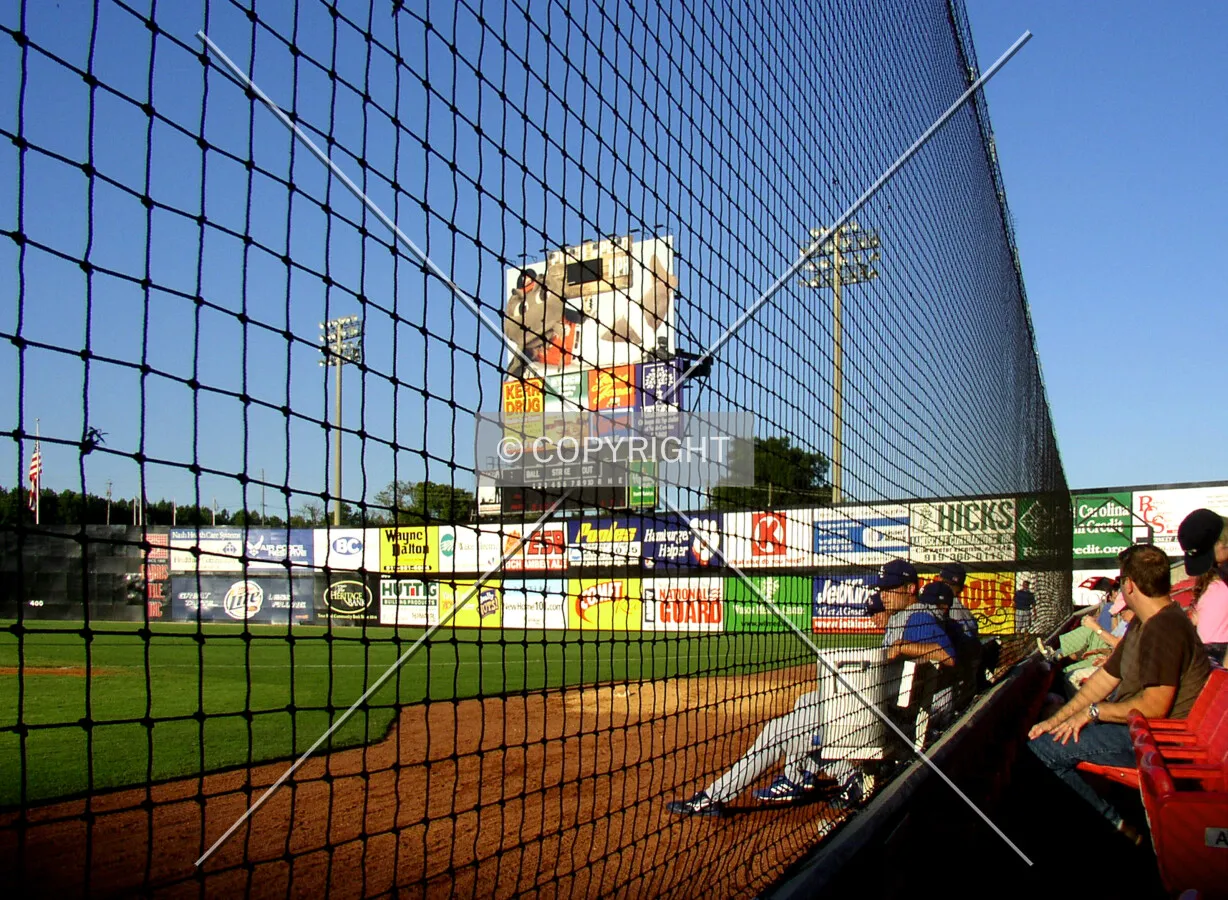 Behind the netting on the first base side