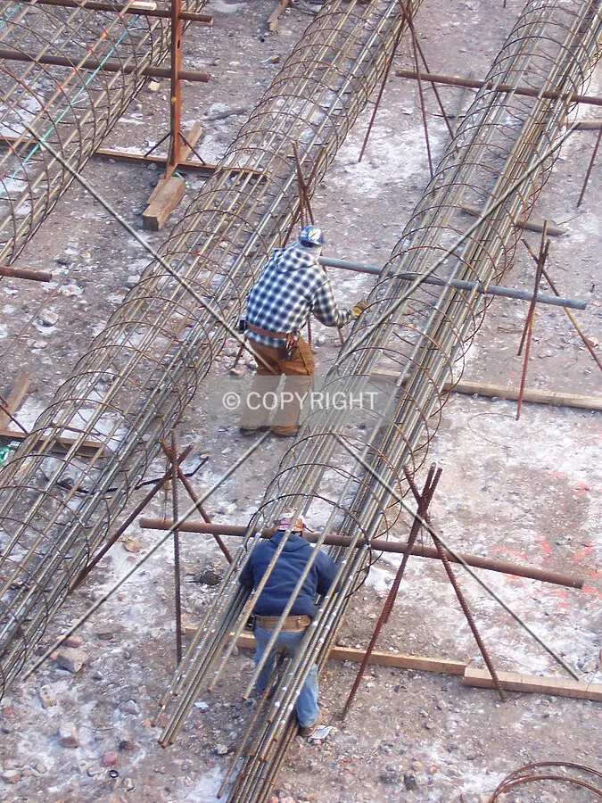 Two workers assembling rebar cages in the northeast corner of the site