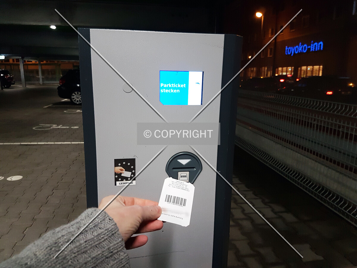 A man is inserting a parking ticket into a ticket machine of a car park