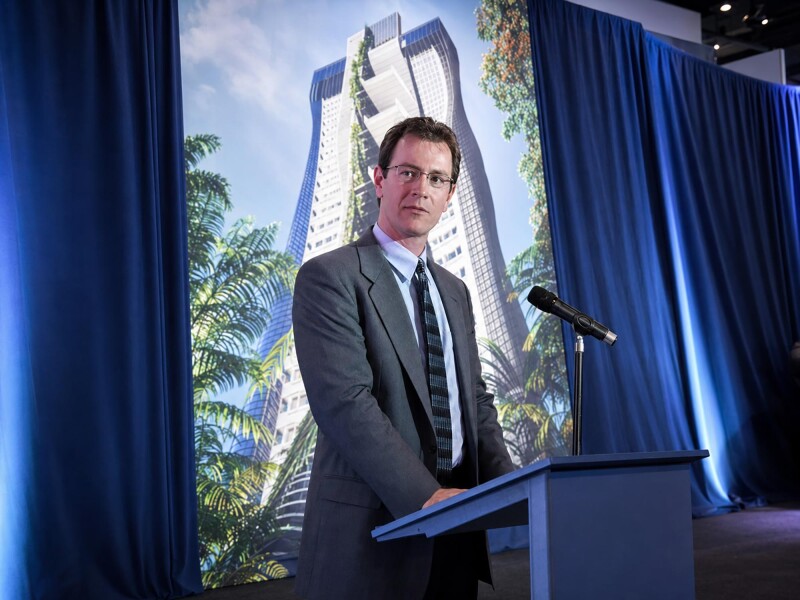 Speaker at a lectern in front of a skyscraper presentation