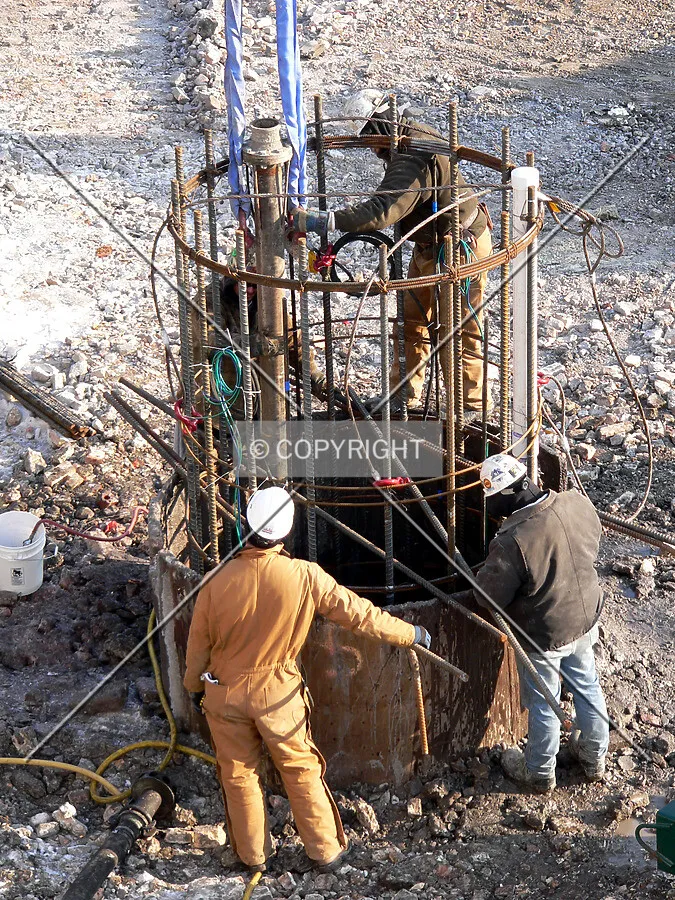 Workers lowering a steel rebar cage down a caisson hole